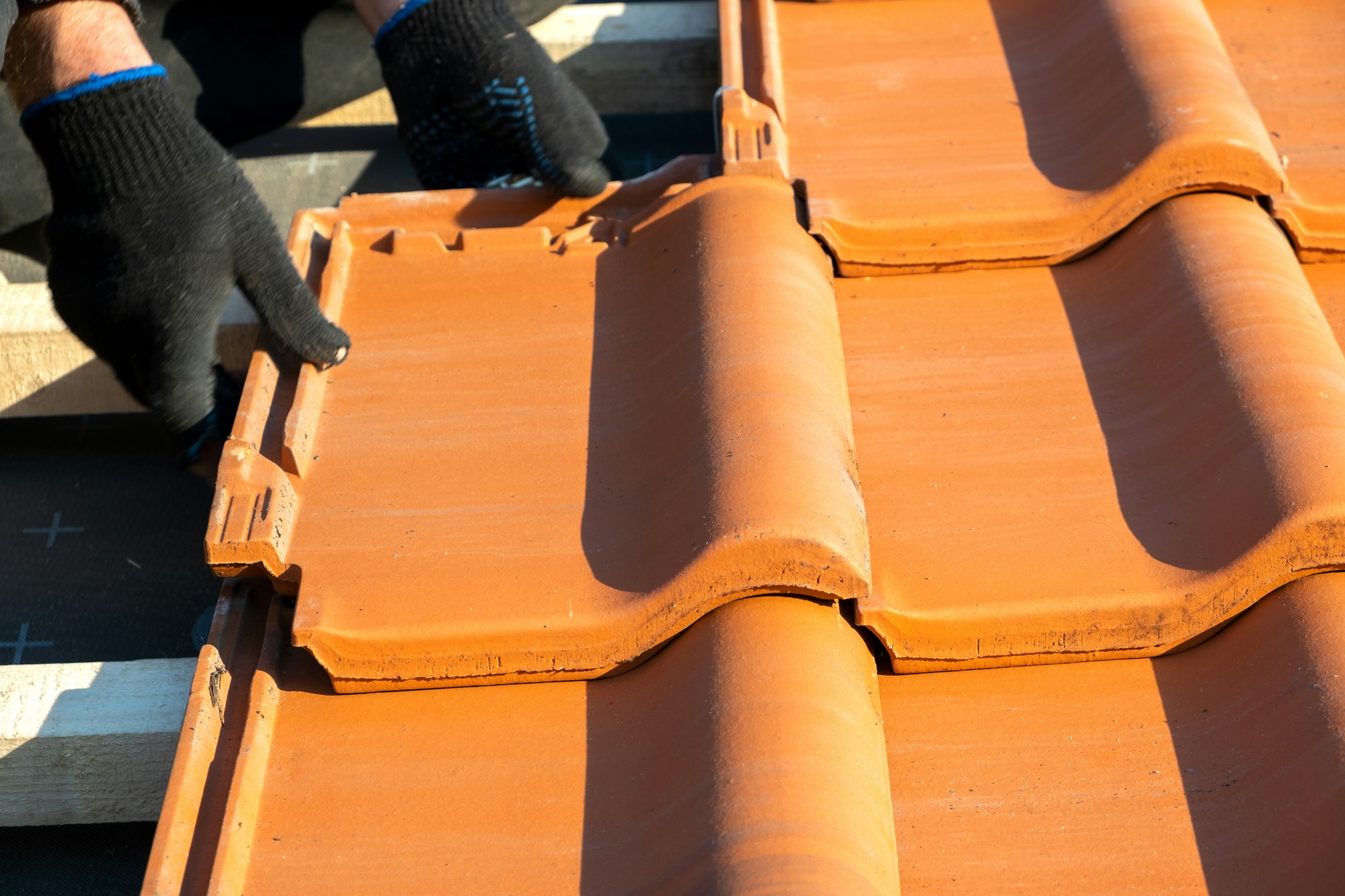 Closeup of worker hands installing yellow ceramic roofing tiles mounted on wooden boards covering